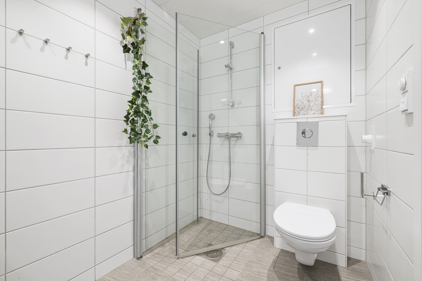 Badet er innredet med heldekkende servant, speil og lysarmatur over servant, veggmontert klosett, dusjhjørne med svingdører og termostatstyrt blandebatteri. Det er opplegg for vaskemaskin. Galleribilde