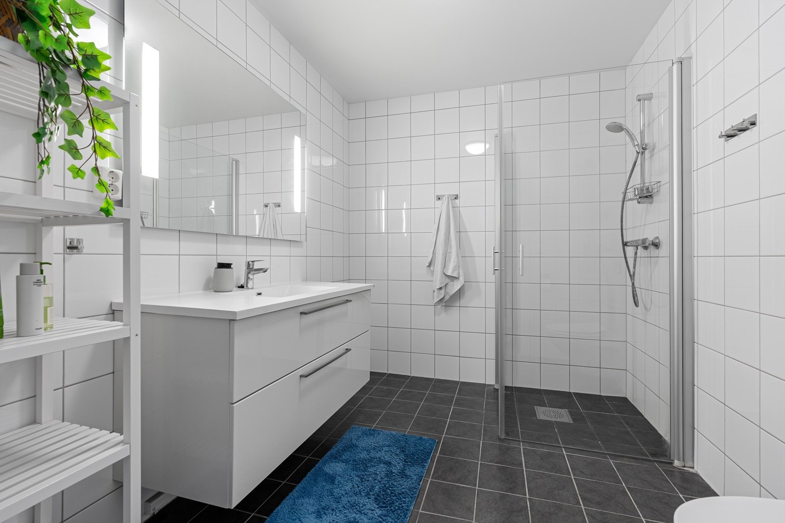 Badet er også av god størrelse. Det er helfliset med varme i gulvet. Det inneholder et vegghengt toalett, baderomsinnredning med speil over, samt innfellbare dusjdører. Galleribilde