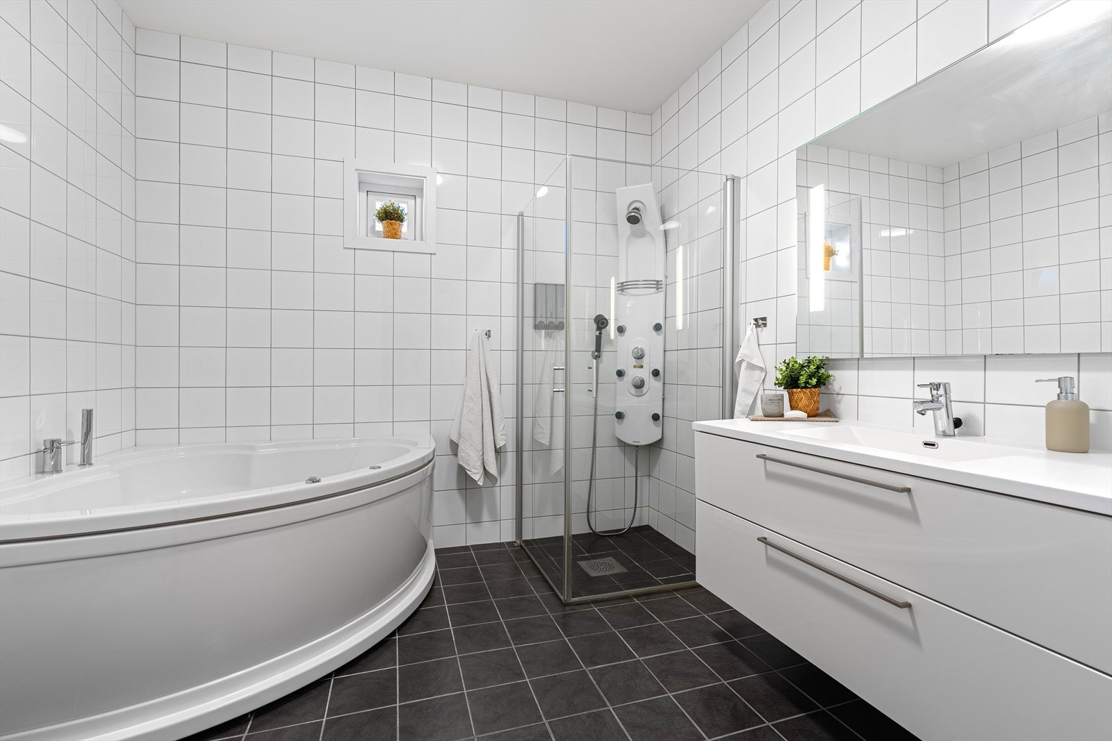 Badet i 1.etg. er helfliset med varme i gulvet. Det inneholder et større hjørnebadekar, innfellbar dusjnisje, vegghengt toalett, samt baderomsinnredning med speil over. Galleribilde