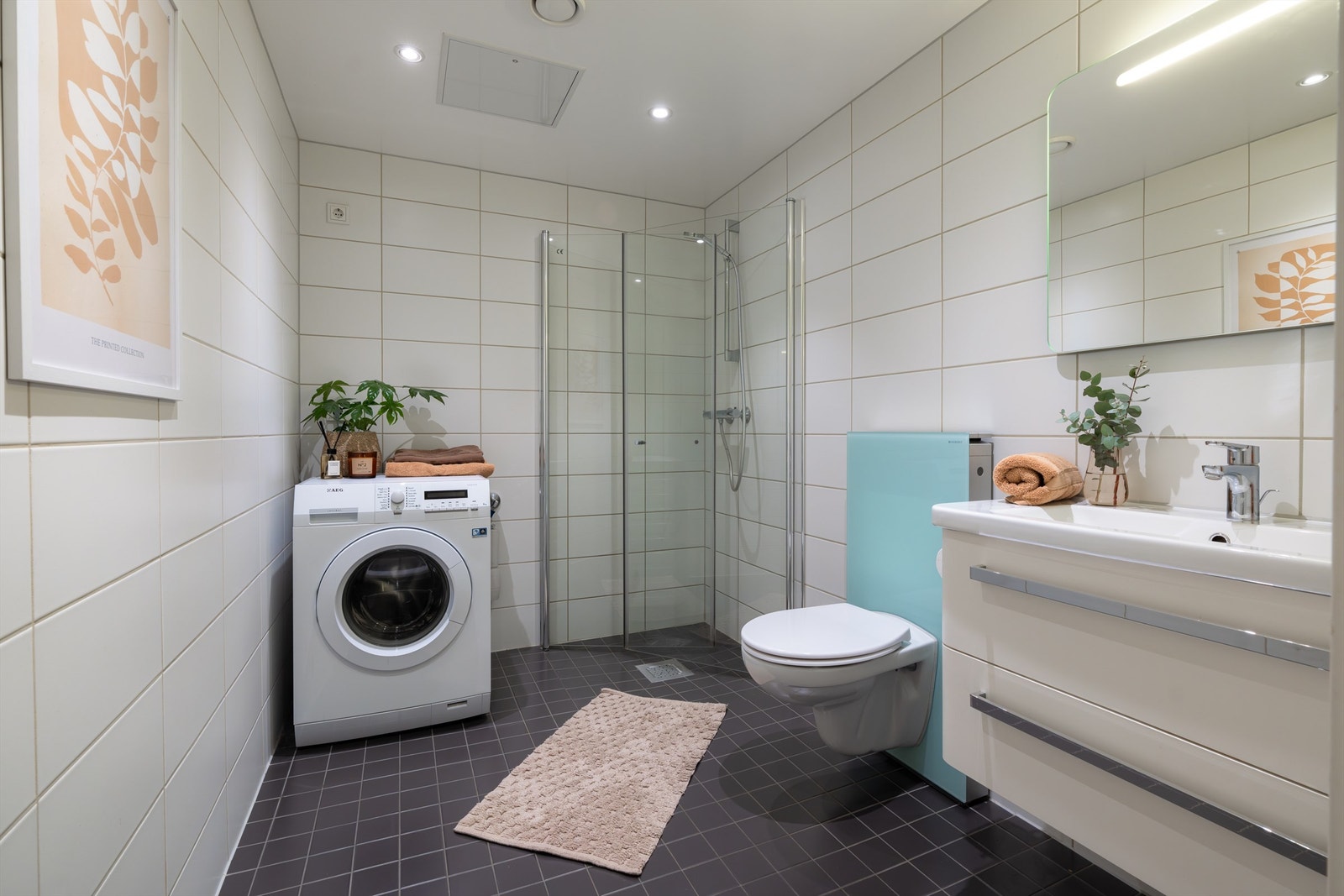 Boligen har et innbydende bad med inngang fra entréen. Badet er bygget opp med hvite fliser på vegg, mørke fliser på gulv, gulvvarme og downlights i tak. Galleribilde