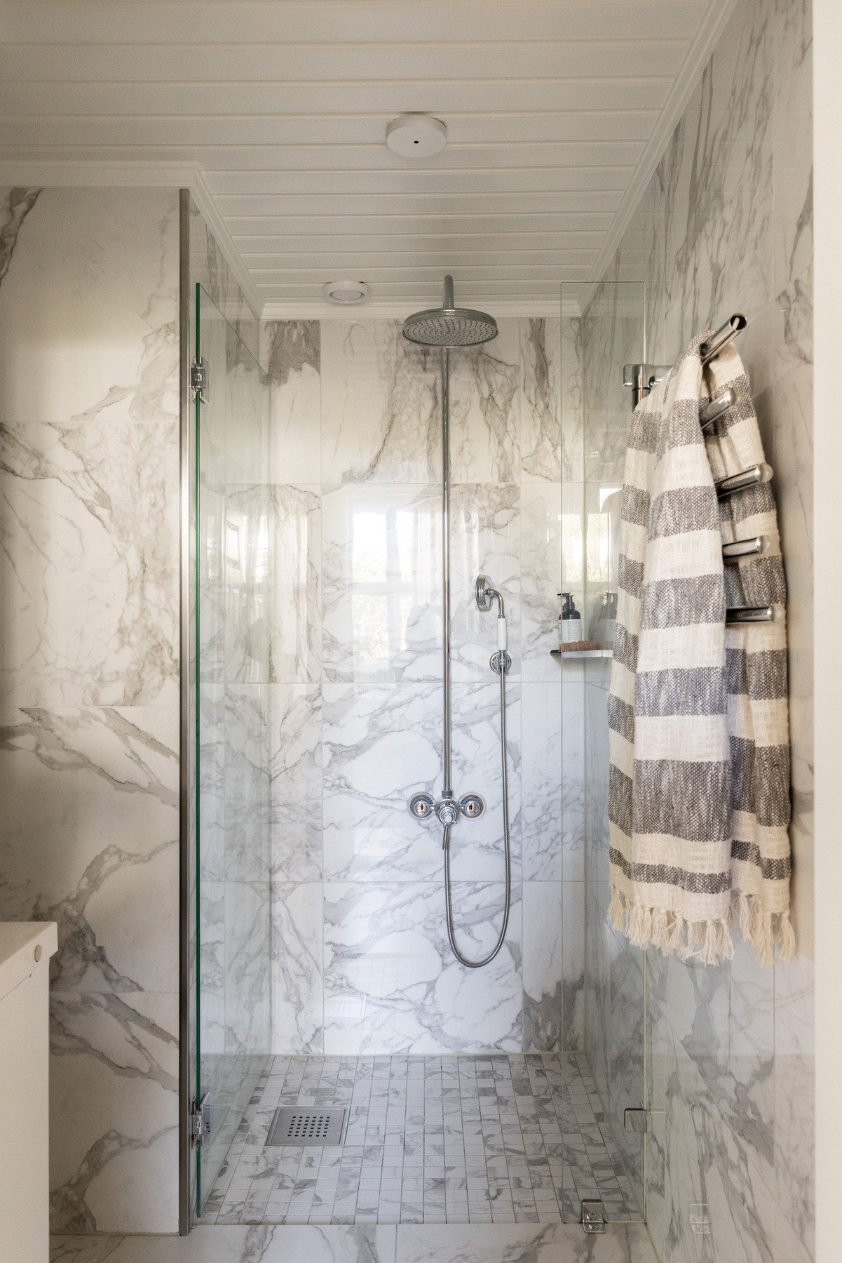 Badet er stilfullt innredet med fliser i marmorlook, dusjhjørne med glassvegg, moderne servantinnredning og håndkletørker. Galleribilde