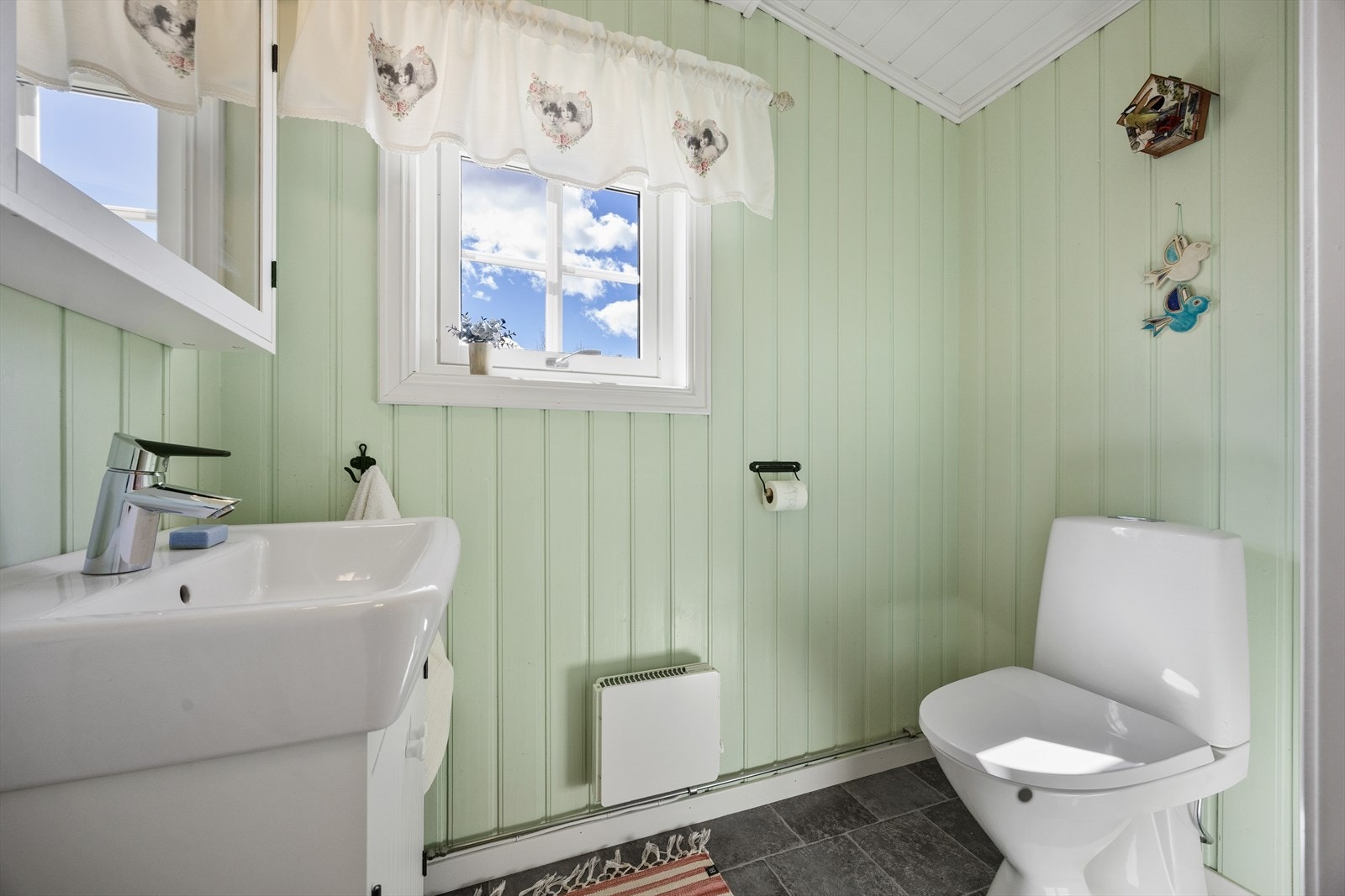 WC-rommet har malt panel på veggene og grått belegg på gulvet, og i tillegg til et toalett har rommet en hvit servantseksjon. Galleribilde