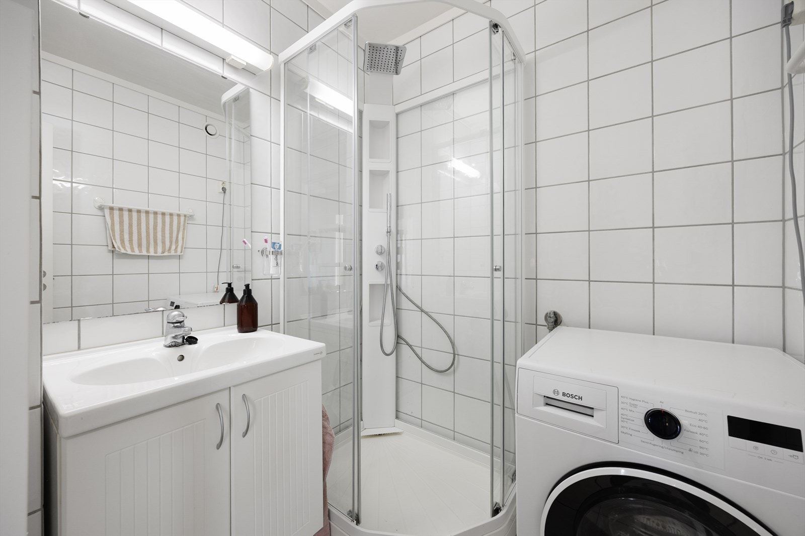Badet er flislagt og utstyrt med dusjkabinett, servantinnredning og opplegg for vaskemaskin. Galleribilde
