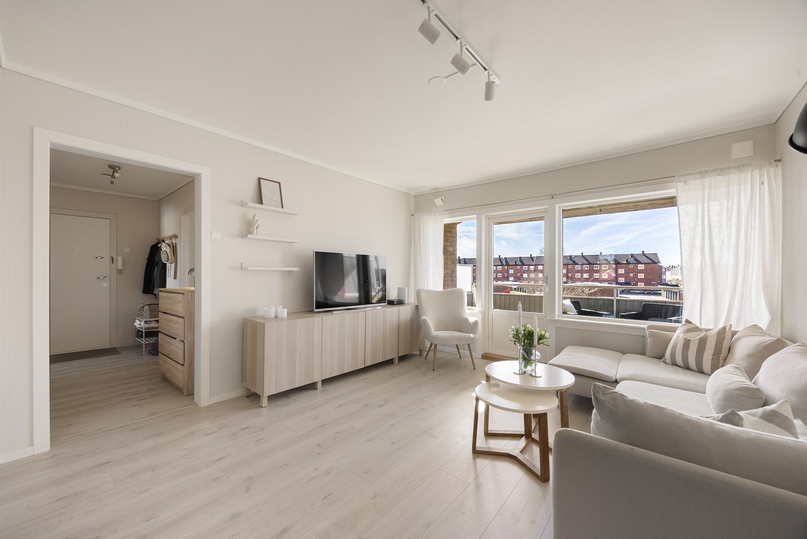 De lyse overflatene og det nye laminatgulvet skaper en helhetlig og tidsriktig atmosfære i stuen. Fra stuen er det en åpen og naturlig flyt mot gangen og resten av leiligheten. Galleribilde