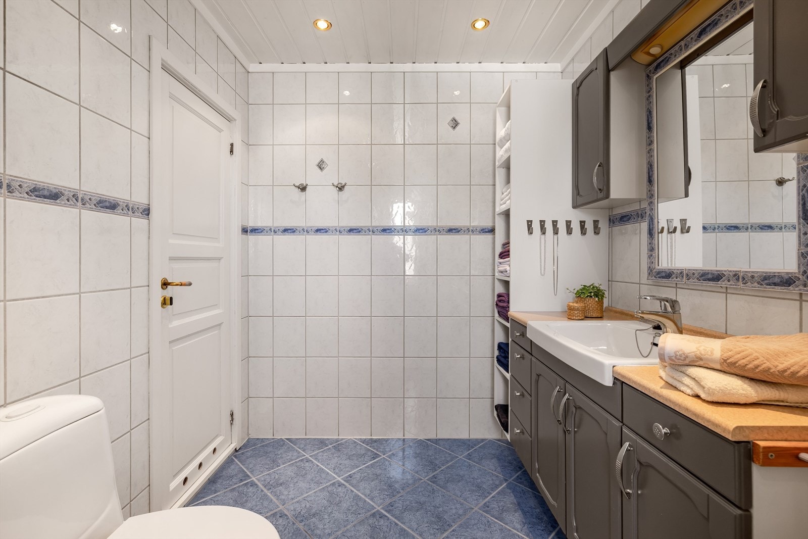 Badet har gulvmontert toalett og en romslig baderomsinnredning med underskap og veggskap. Benkeplate med servant. I overkant er det speil og lys. Galleribilde