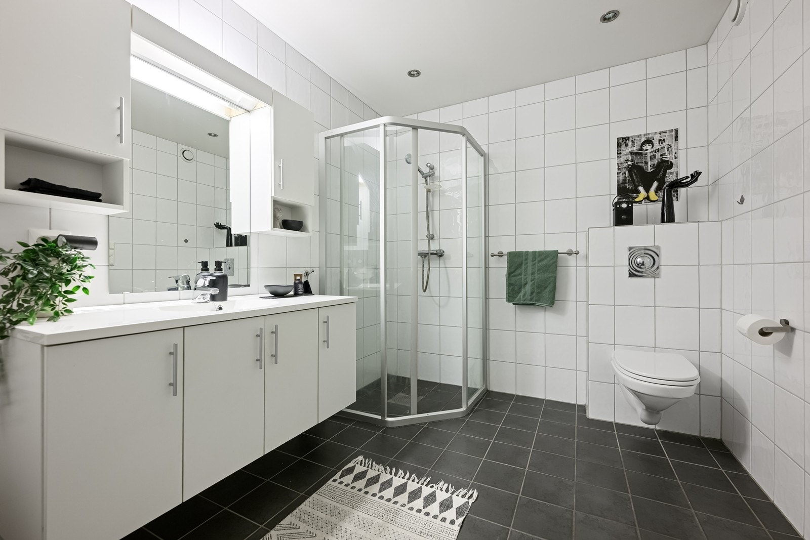 Badet er flislagt på gulv og vegger og er utstyrt med servant med innredning, vegghengt toalett og dusjløsning Galleribilde