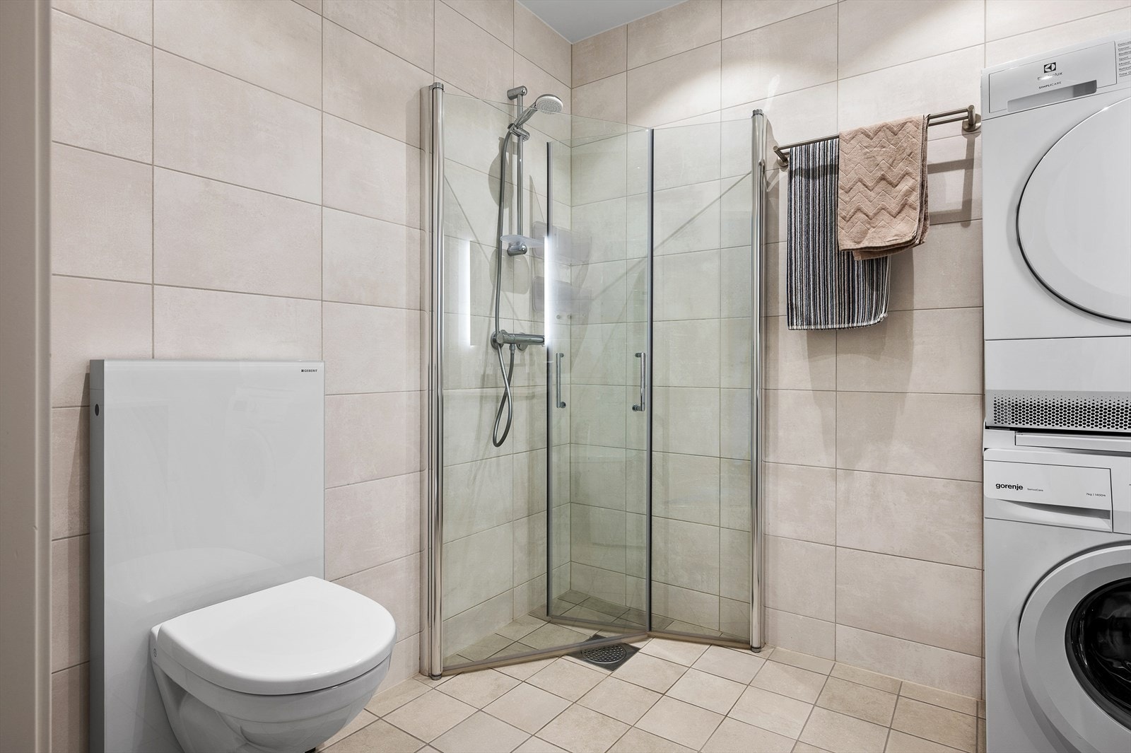 Badet er utstyrt med vegghengt toalett, dusjhjørne, moderne baderomsinnredning og opplegg for vaskemaskin. Galleribilde