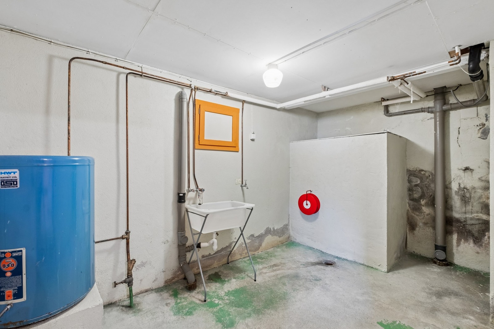 Vaskerom med betonggulv og vegger. Utslagsvask i plast. Varmtvannstank plassert her. Galleribilde