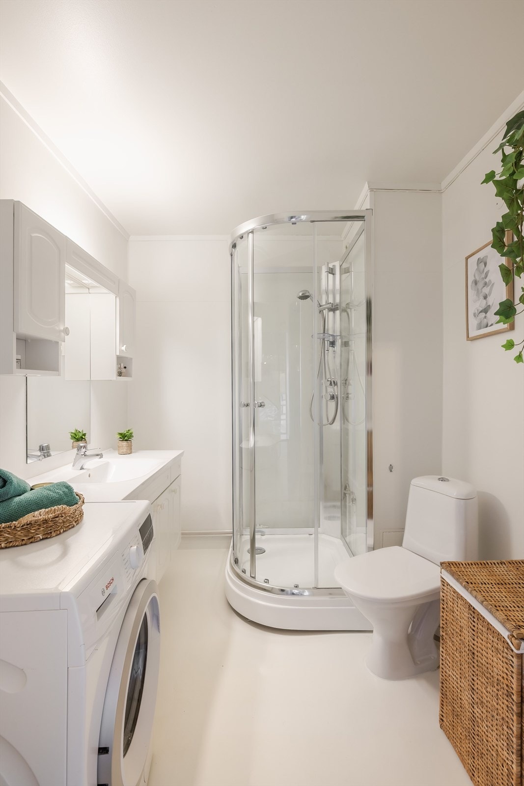 Lyst bad med malt vinylbelegg på gulv og vegger. Badet har gulvmontert toalett, dusjkabinett og opplegg for vaskemaskin. Galleribilde
