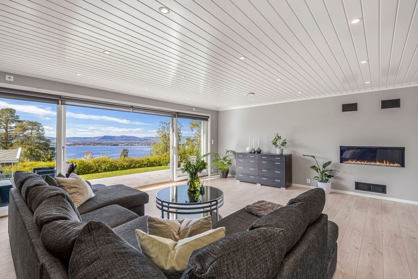 Boligens stue er et imponerende oppholdsrom med store panoramavinduer som rammer inn den spektakulære utsikten mot sjøen og slipper inn rikelig med naturlig lys. Galleribilde