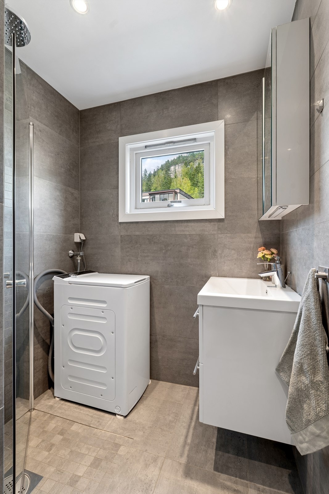 Badet er innredet med nedfelt servant, speilskap, dusjhjørne med innfellbare dusjdører, vegghengt toalett og opplegg for vaskemaskin. Galleribilde