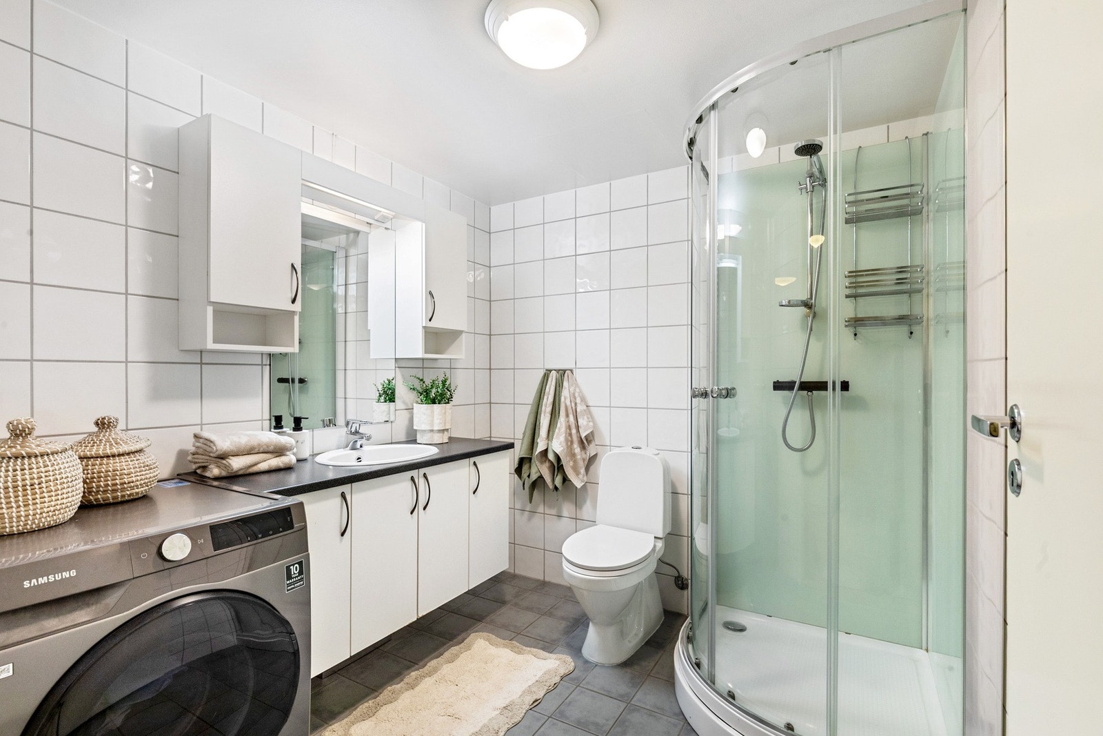 Flislagt baderom med varme i gulv- baderommet er utstyrt med mekanisk avtrekk, opplegg for vaskemaskin, servant, servantskap, dusjkabinett og wc. Galleribilde
