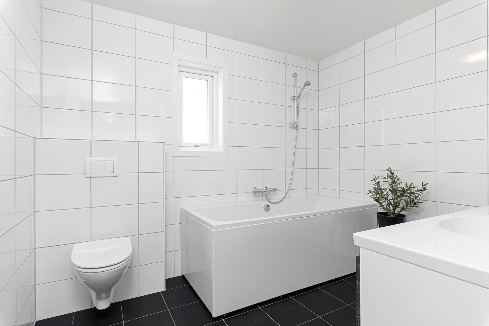 Badet i 2. etasje er helfliset og stilrent utformet, med nedfelt servant i skuffeseksjon, badekar og vegghengt toalett. Galleribilde