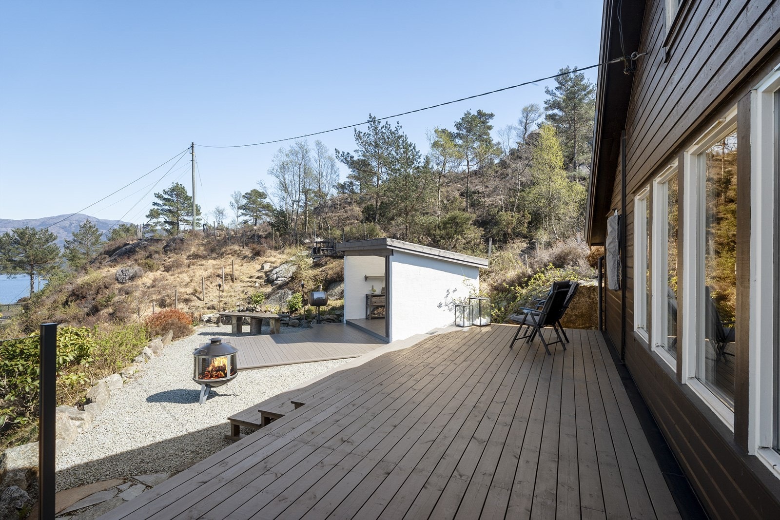 Stor terrasse i front av hytten (anlagt i 2025). Trapp ned til gapahuk. Med så mange uteplasser på eiendommen kan dere enkelt flytte dere etter solen. Galleribilde