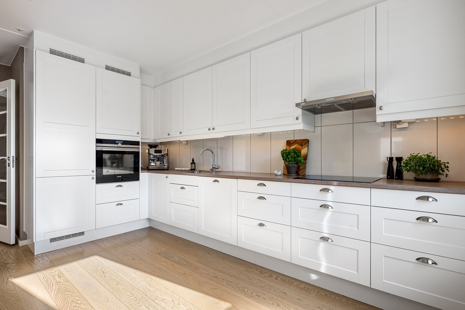 Lekkert og romslig innredet med hvite profilerte fronter, laminert benkeplate og nedfelt vaskekum. Her får du godt med skap- og arbeidsplass, samtidig som løsningen er praktisk og funksjonell i hverdagen. Galleribilde