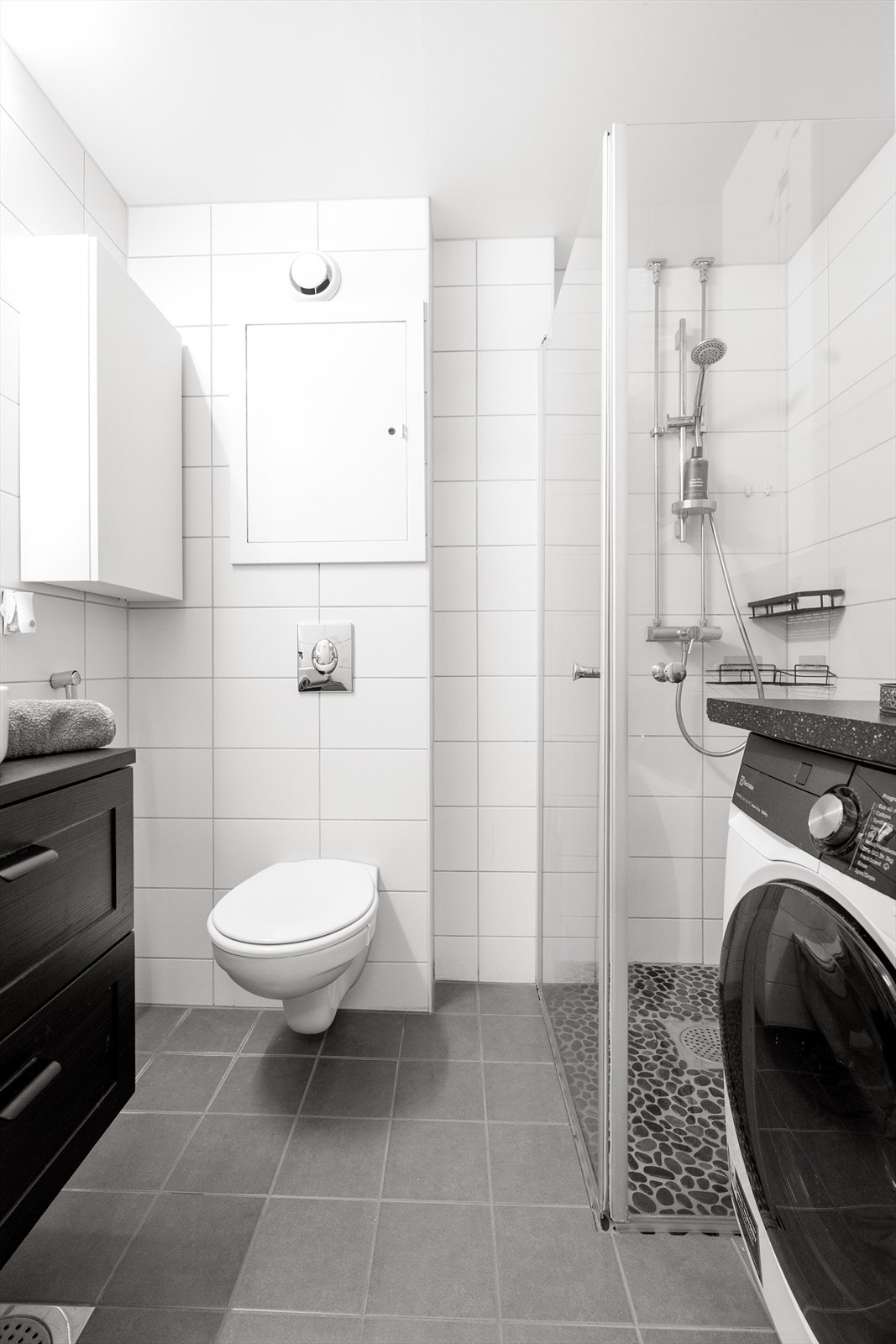 Badet er utstyrt med vegghengt toalett og et dusjhjørne med inn- og utadslående dører i herdet glass. Galleribilde