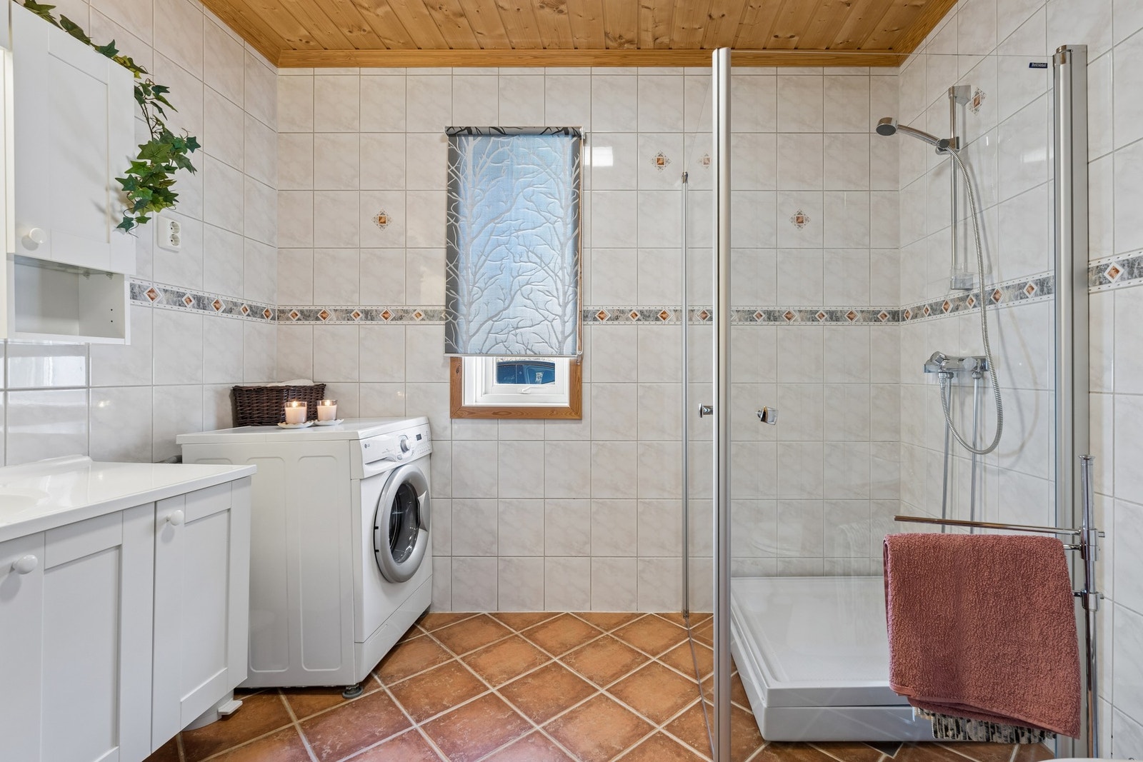 Rommet har en dusjnisje med kabinettbunn og glassvegger, gulvmontert vannklosett, baderomsinnredning med malte fronter og helstøpt servantplate, samt vann- og avløpsinstallasjoner for vaskemaskin. Galleribilde
