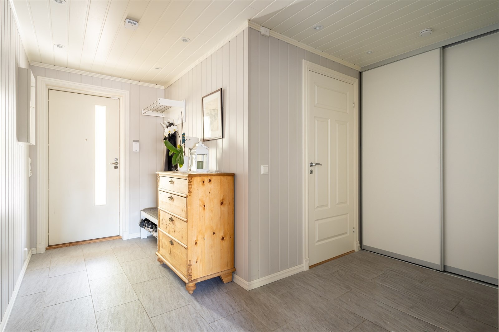 Romslig entré med flislagt gulv, termostatstyrt gulvvarme og skyvedørsgarderobe. Galleribilde