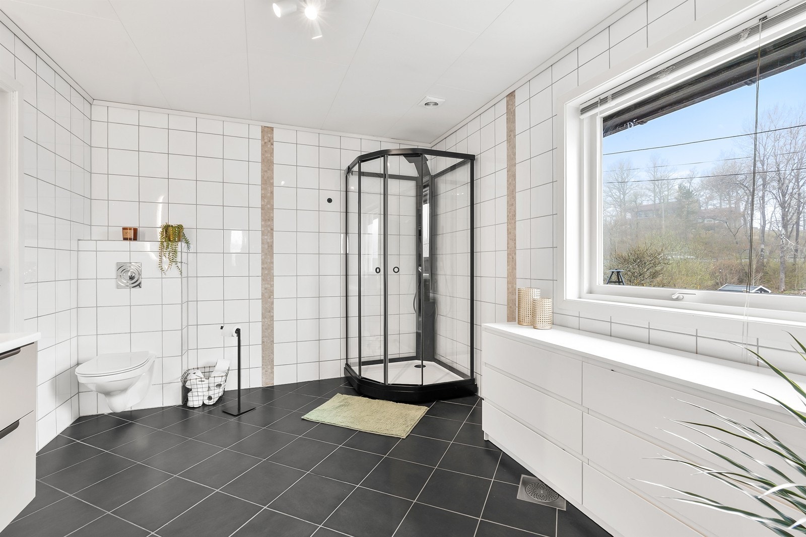 Badet er innredet med baderomsinnredning med servant, dusjkabinett og vegghengt toalett. Det er fliser på gulv og vegger. Galleribilde