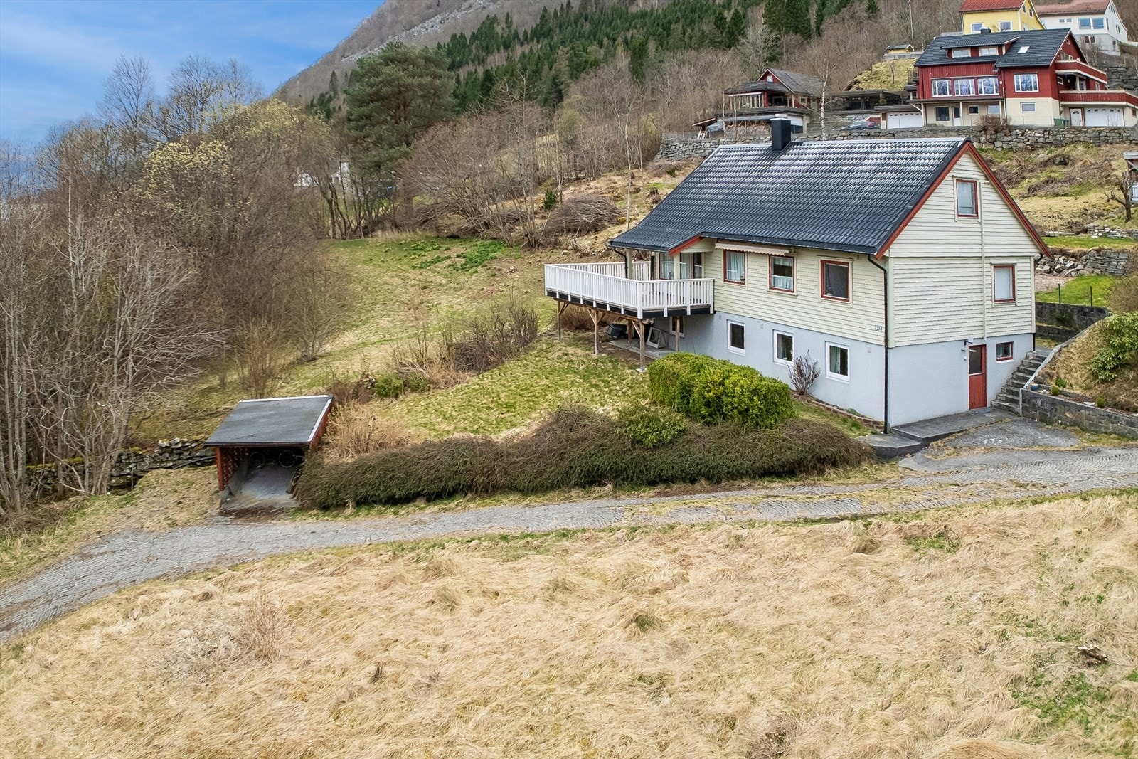 Einebustaden frå 1960 ligg i skrånande terreng, med carport og opparbeida tomt. Galleribilde