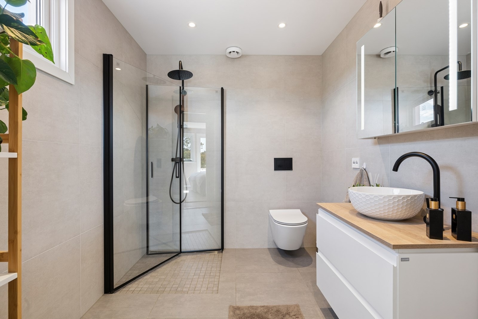 Like ved ligger et stilrent bad, renovert i 2023 med fliser på vegger og gulv, vegghengt toalett, dusjnisje med glassdører og moderne baderomsinnredning. Badet er utstyrt med varmekabler og mekanisk ventilasjon. Galleribilde