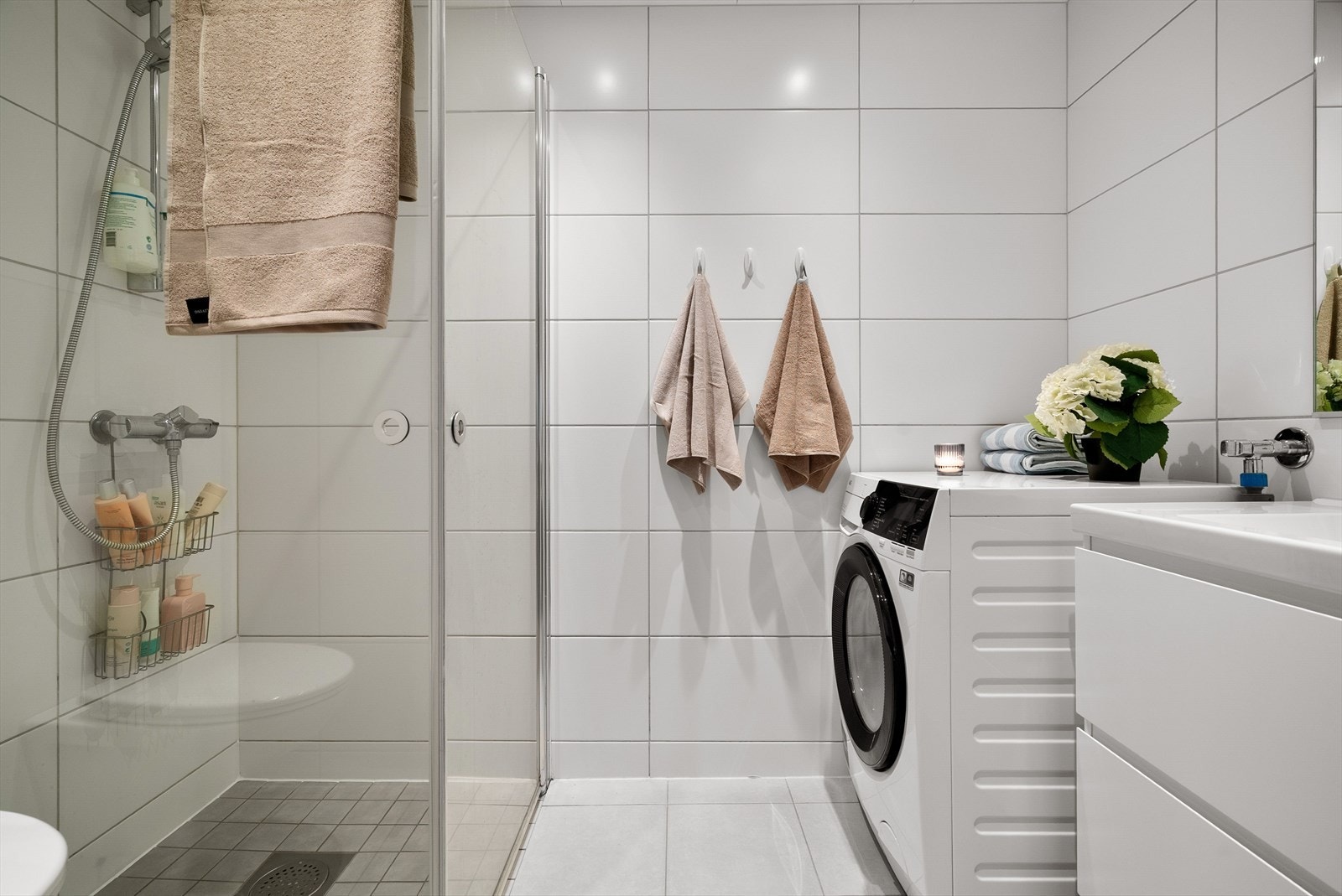 Lyst og moderne baderom utstyrt med servantinnredning, speil, toalett, dusjhjørne og opplegg for vaskemaskin. Galleribilde
