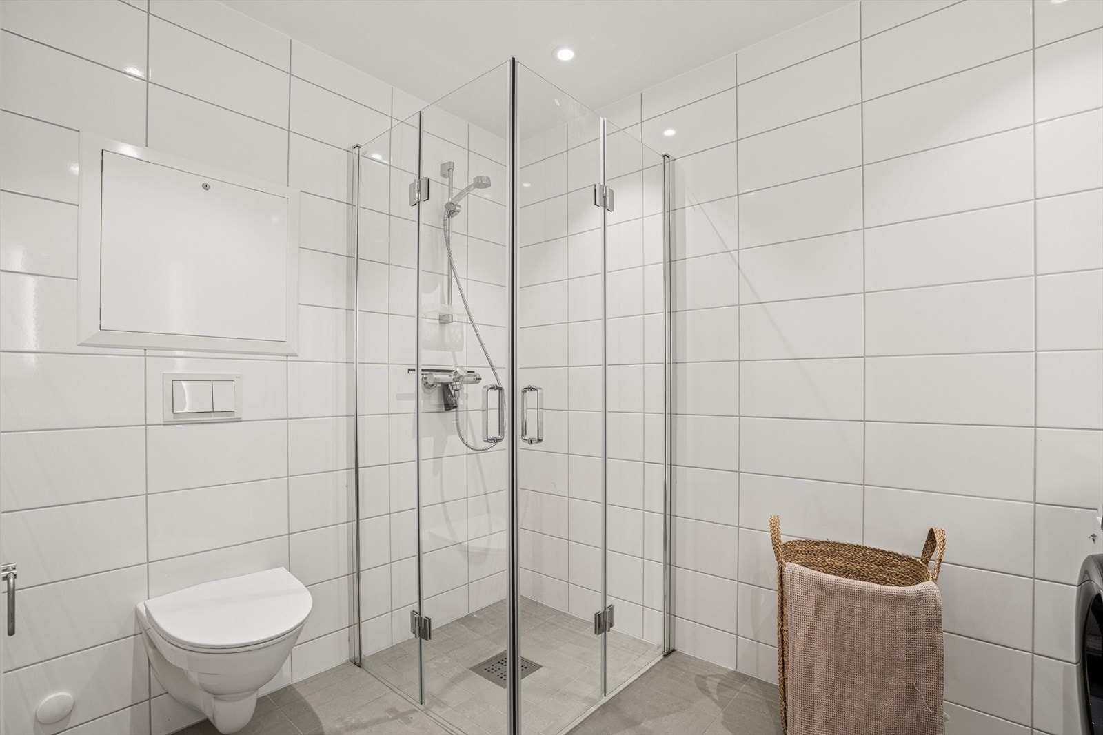 Badet er utstyrt med vegghengt toalett, servant, opplegg til vaskemaskin og tørketrommel samt dusjhjørne Galleribilde