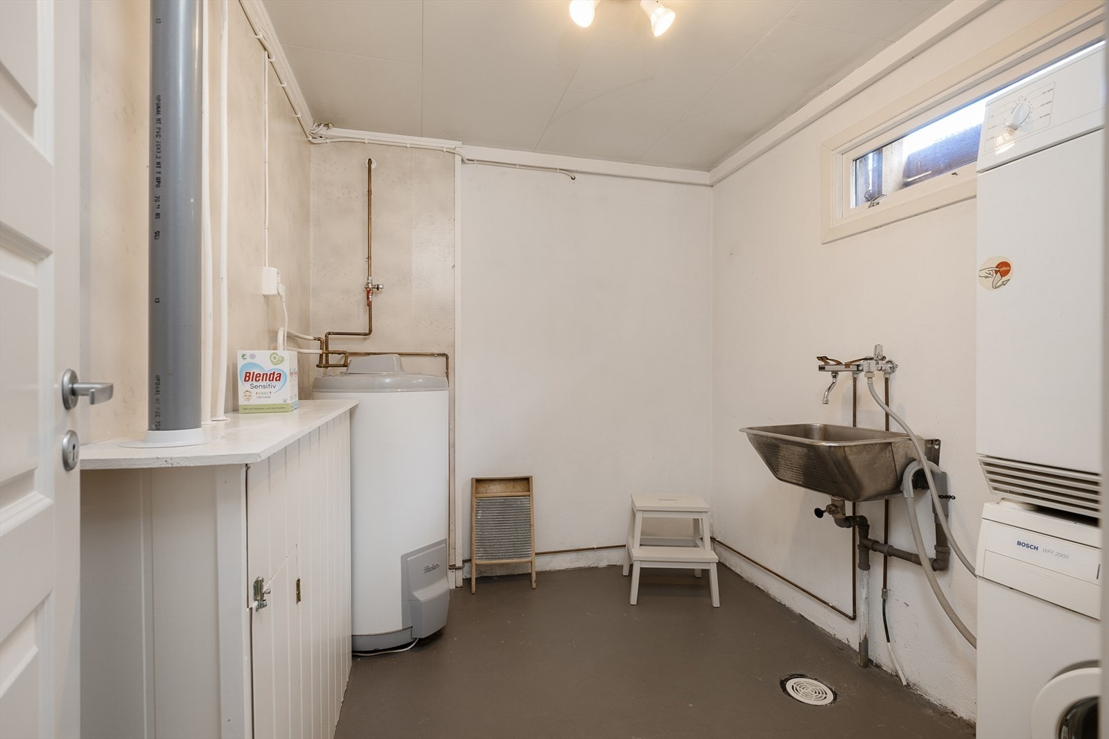 Praktisk vaskerom med malt betonggulv, sluk og opplegg for vaskemaskin. Her er også boligens stoppekran og en 200-liters varmtvannsbereder. Rommet er av takstmann gitt TG3. Galleribilde