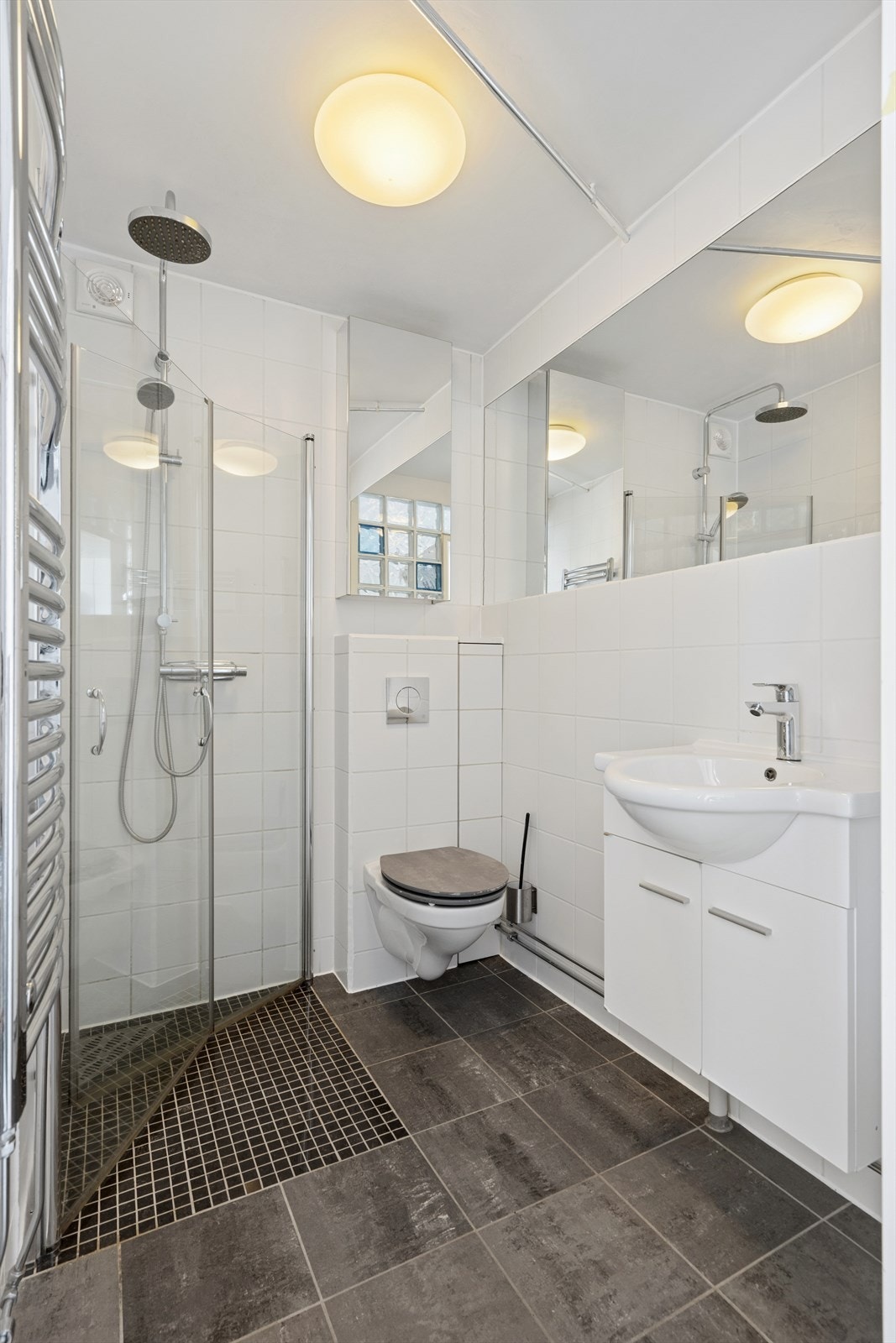 Badet er utstyrt med dusj, wc og servant med skap. Stort speil på vegg Galleribilde