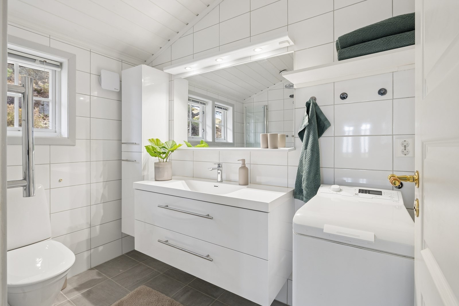 Rommet er utstyrt med servantinnredning, høyskap, speil, vegghengt toalett, dusjhjørne med glassdører og opplegg for vaskemaskin. Galleribilde