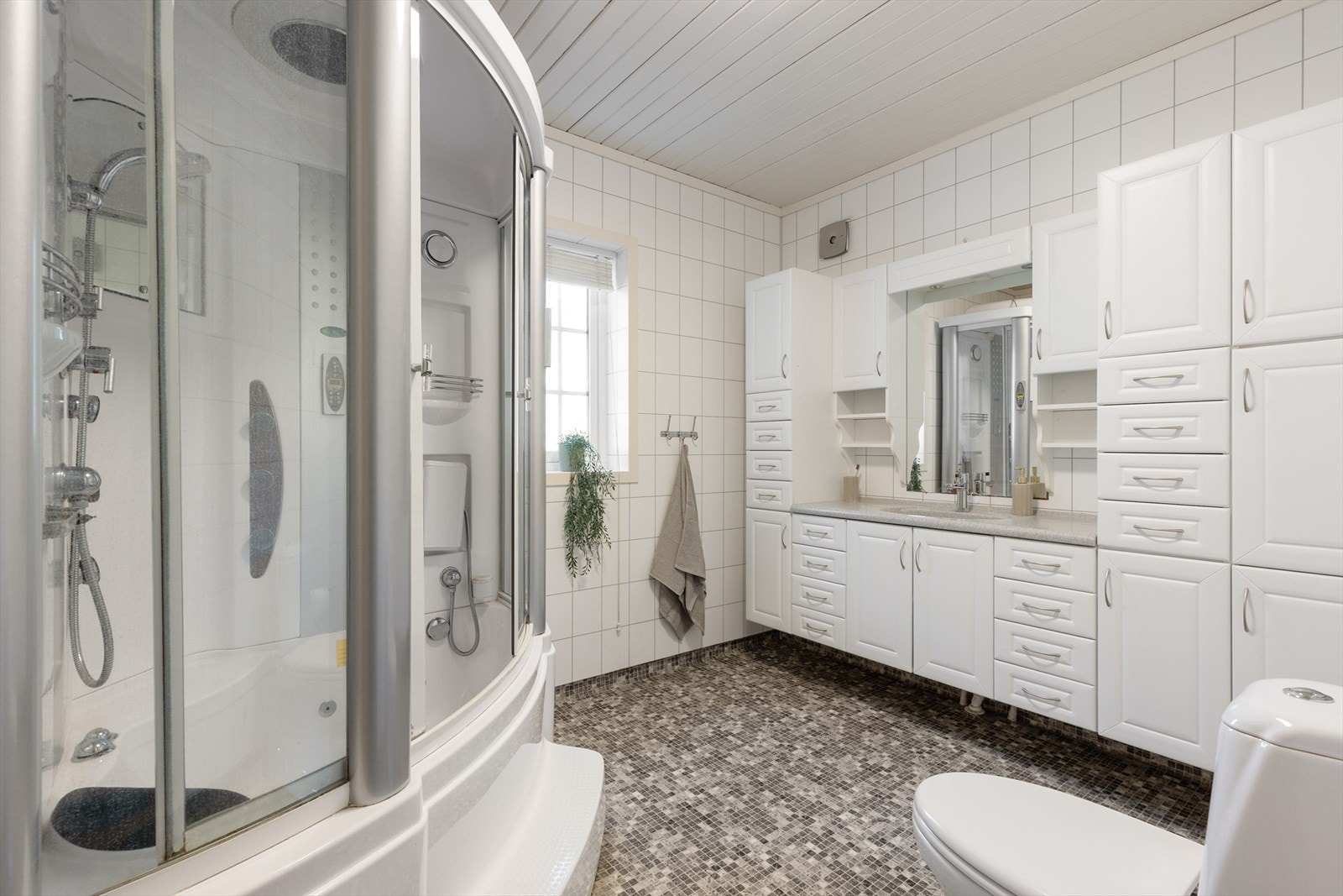 Romslig bad med rikelig skapplass, gulvmontert toalett og et dusjkabinett med badekar. Det er belegg på gulv og våtromsplater på vegger. Galleribilde