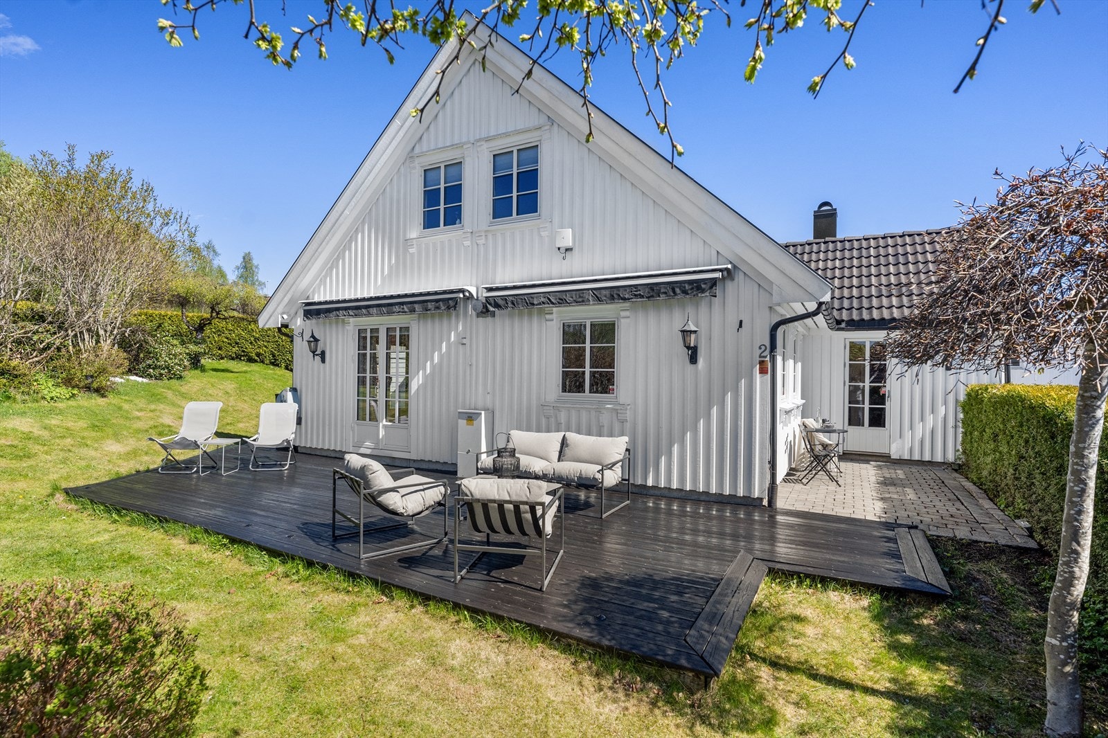 Terrassen strekker seg rundt deler av husveggen og gir flere soner for møblering med loungegruppe, solstoler og grill. Det er montert to markiser ved terrassen. Galleribilde