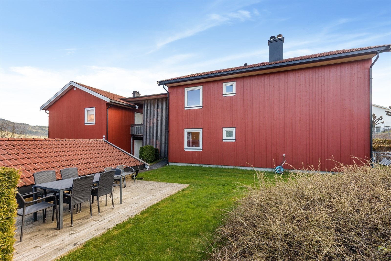 Fra borettslagets fellesområder, med felles platting og sittegruppe. Inngang til leiligheten via utvendig trapp (bak spilene). Galleribilde