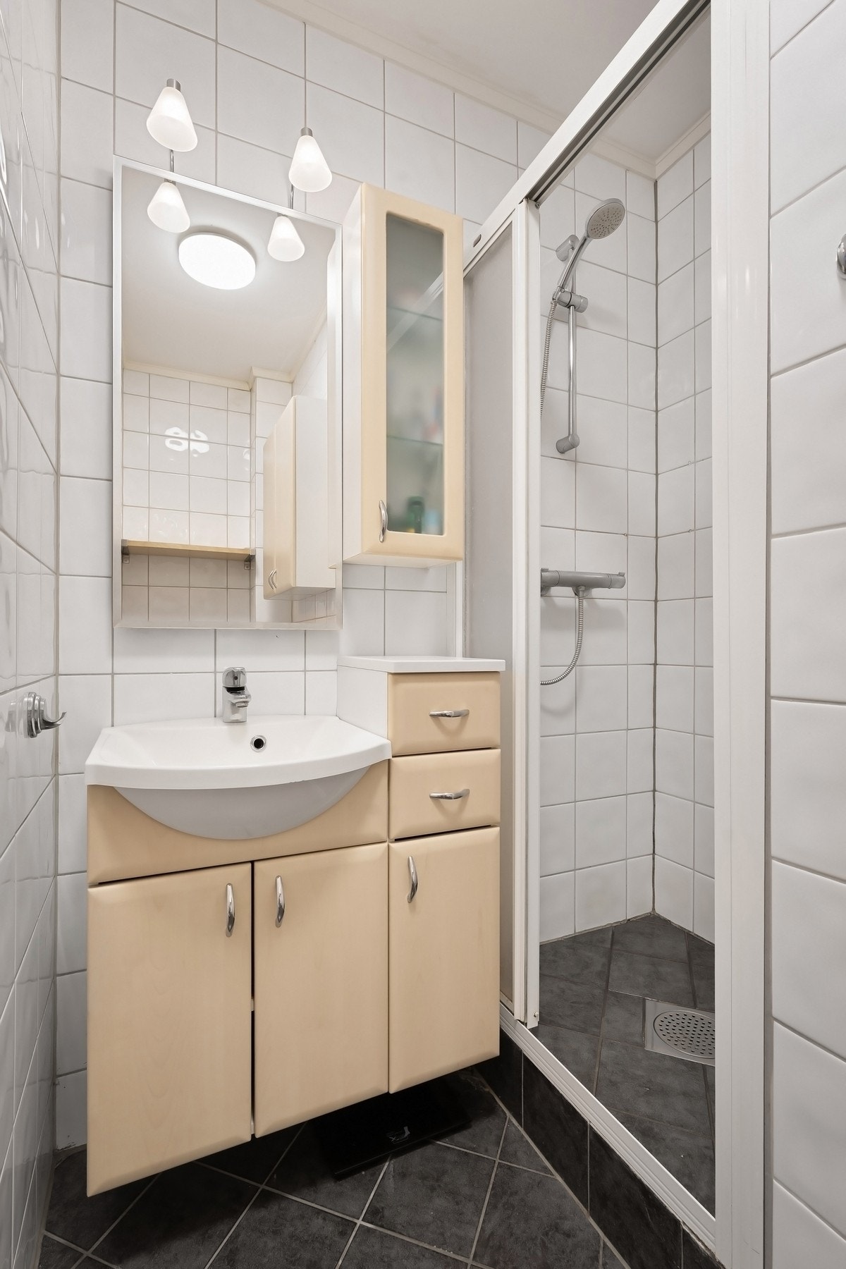 Badet er innredet med vegghengt servantinnredning med dører, ovenpåliggende servant, speil med overlys, dusjhjørne med dører, samt gulvstående toalett. Galleribilde