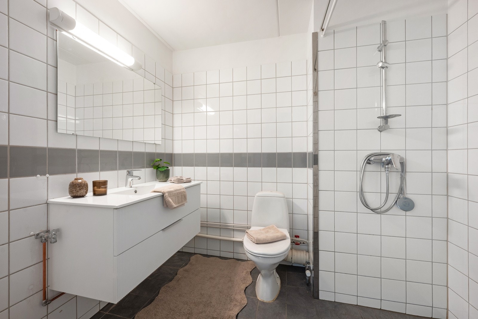 Romslig flislagt bad innredet med servant, speil med lys, toalett og opplegg for vaskemaskin. Galleribilde