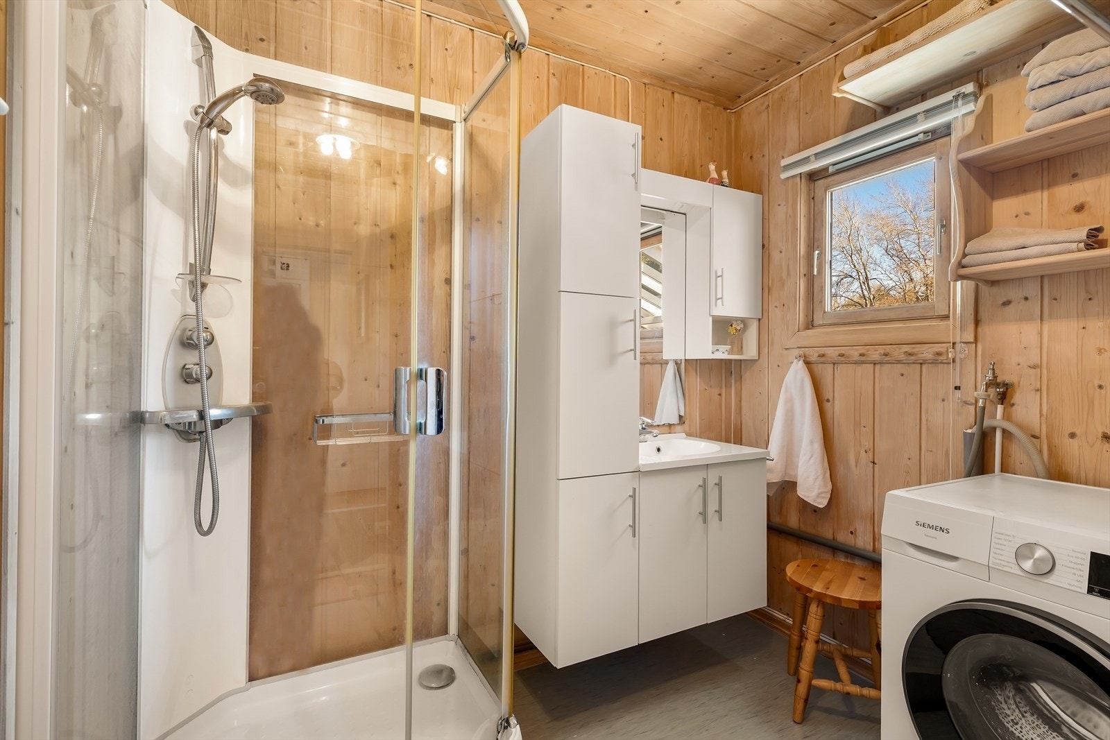 Badet har gulvbelegg, panel på veggene, dusjkabinett, servantinnredning og opplegg for vaskemaskin. Galleribilde
