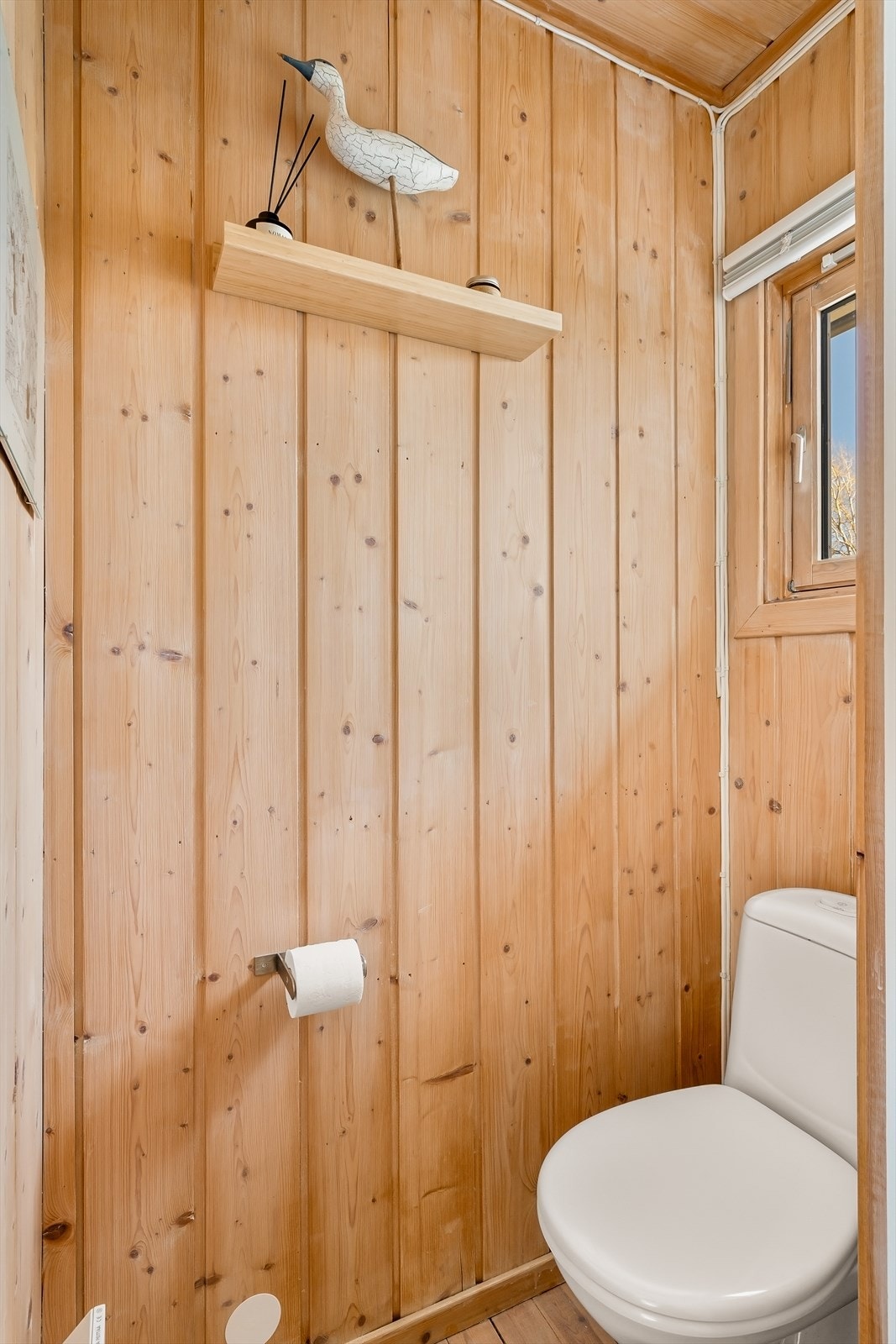 Separat toalettrom med panel på vegger, furugulv og naturlig ventilasjon. Galleribilde