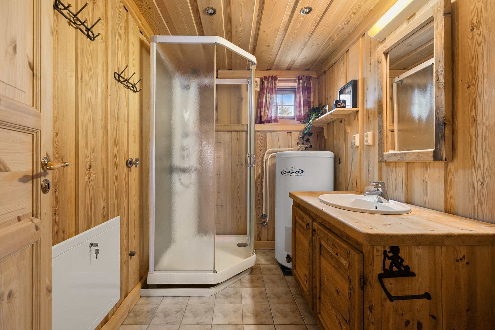 Badet har en lun og tradisjonell utførelse med vegger i panel og tømmer, samt panel i himling som harmonerer godt med hyttens øvrige uttrykk. Gulvet er flislagt og utstyrt med elektriske varmekabler som bidrar til god komfort året rundt. Galleribilde