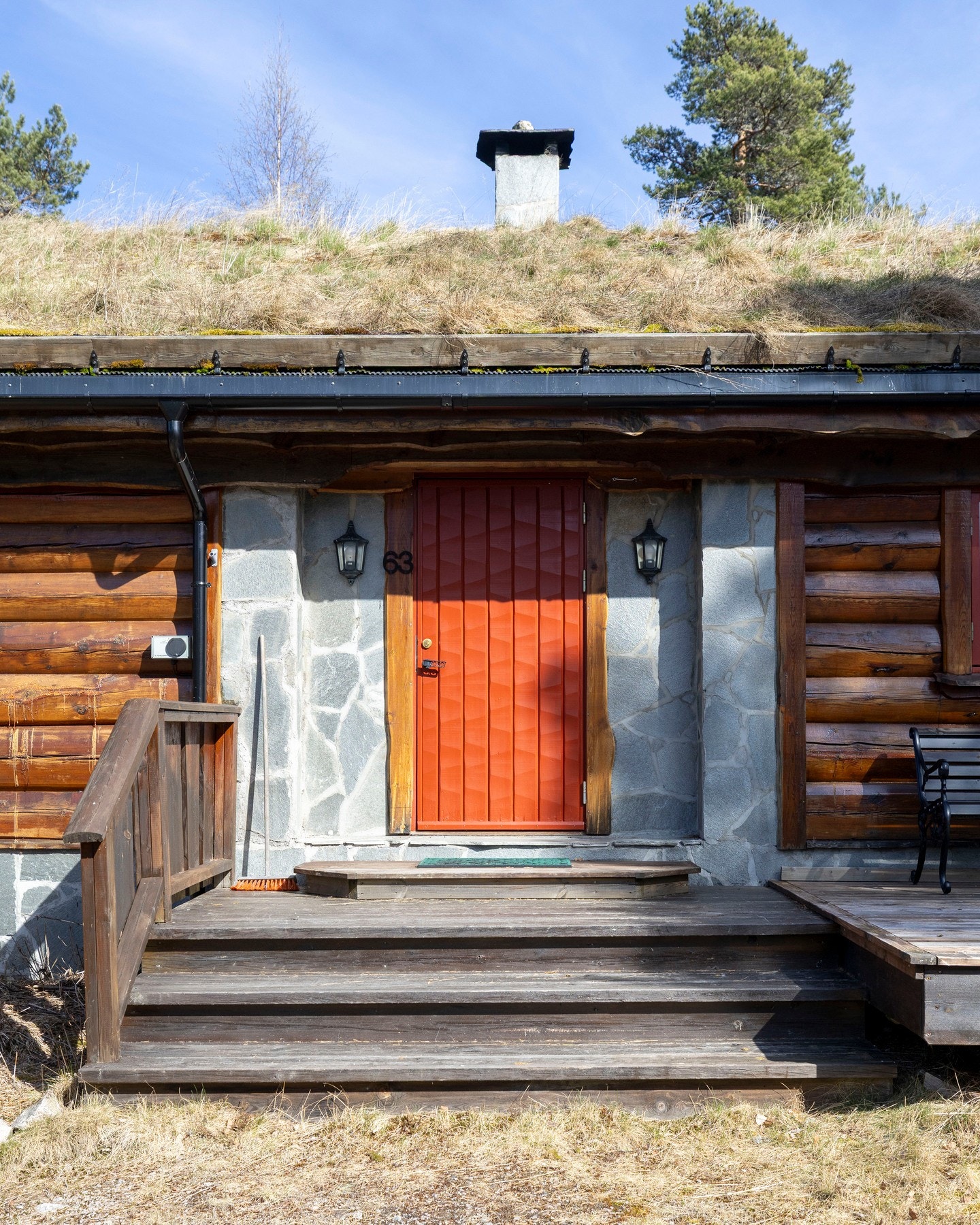 Utvendig møtes man av et hyggelig inngangsparti med torvtak, skiferkledde detaljer og trappeadkomst til terrasse og hovedinngang. Den markerte røde ytterdøren skaper et sjarmerende førsteinntrykk og understreker hyttens klassiske uttrykk. Galleribilde