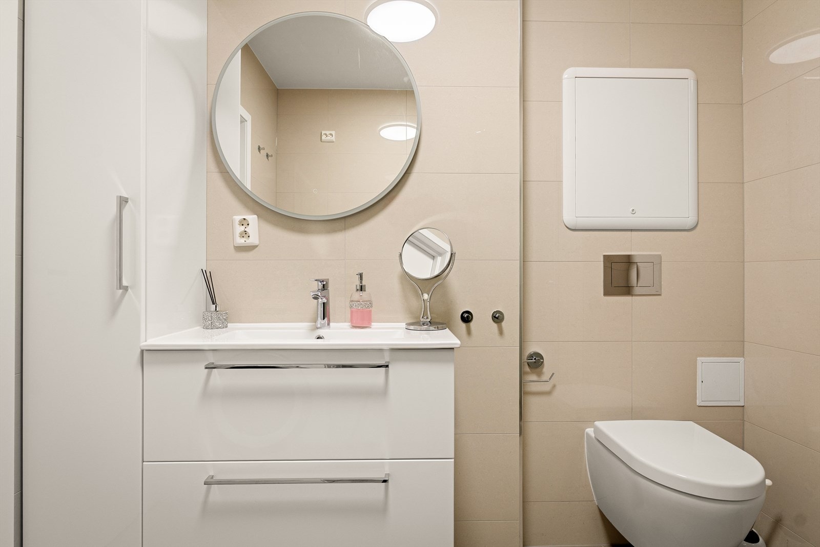 Badet er utstyrt med dusjhjørne, vegghengt toalett, benkeskap med servant og speil med belysning. Galleribilde
