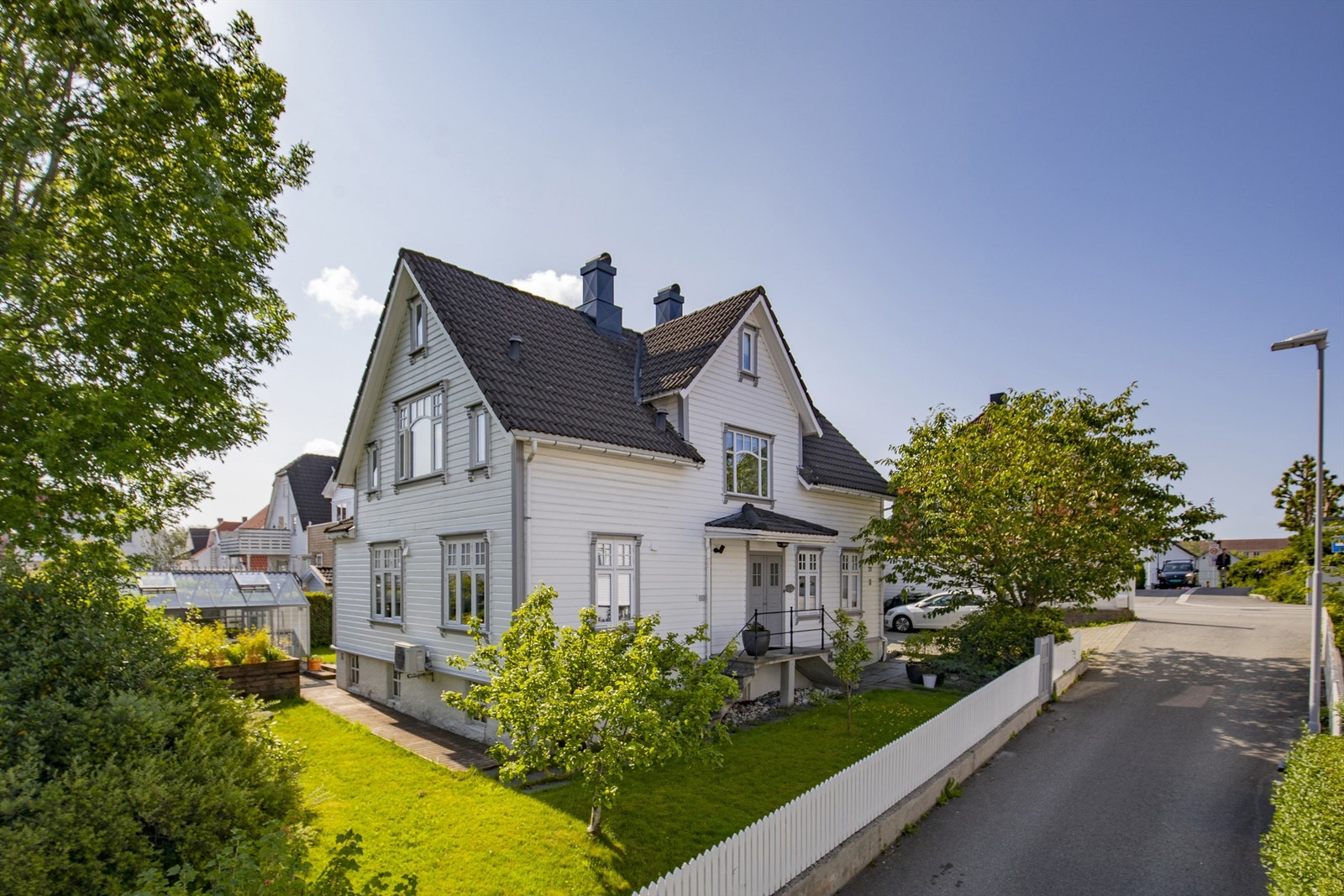 Eiendommen sett fra gaten, med en velholdt hage og hvitt stakittgjerde. Galleribilde