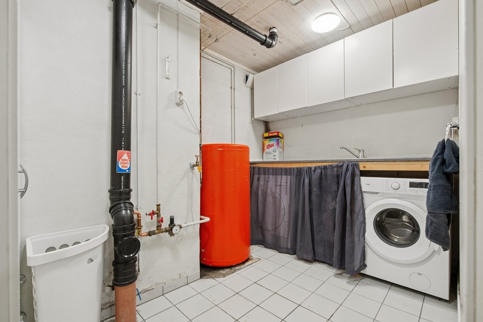 Separat vaskerom i kjelleren med fliser på gulv og opplegg for vaskemaskin. Her er også boligens varmtvannstank på ca. 200 liter plassert. Galleribilde