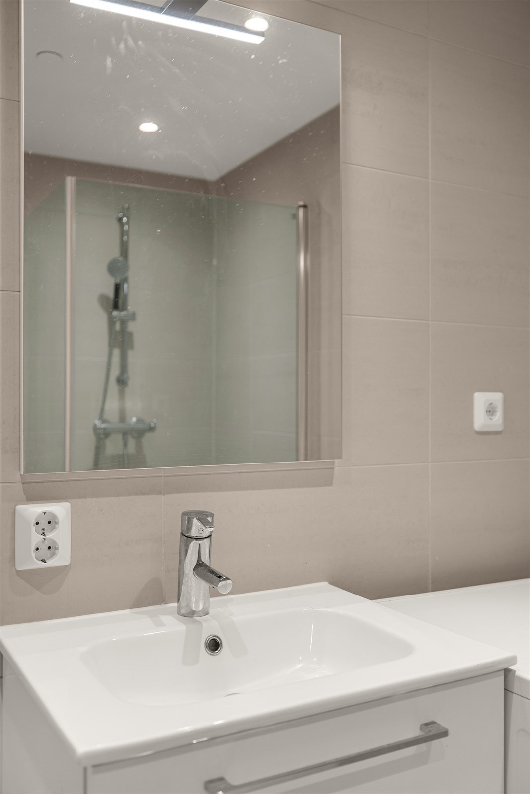 Badet er innredet med vegghengt servant og servantskap, speil med overbelysning, vegghengt toalett og dusjsone med dusjvegger i glasss og dusjarmatur. Galleribilde