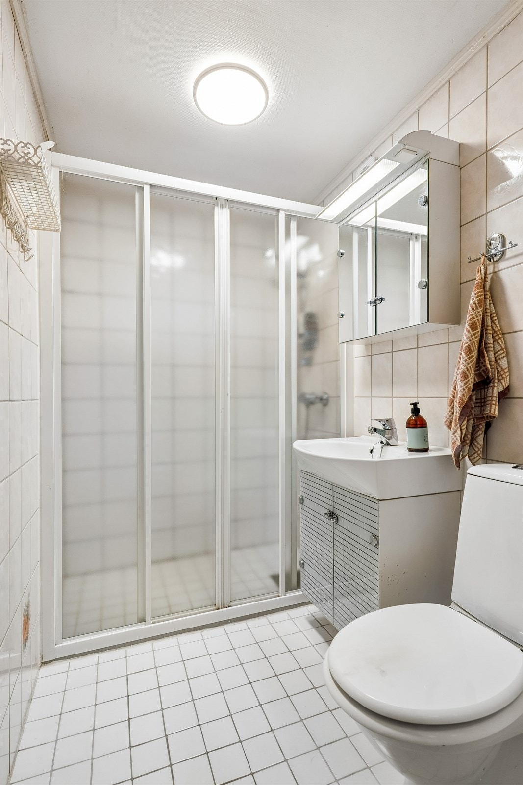 Dette badet ligg vegg i vegg med vaskerommet og er eit lyst flislagt bad med servant, dusj på vegg med sokkellist og varmekablar i golv. Galleribilde