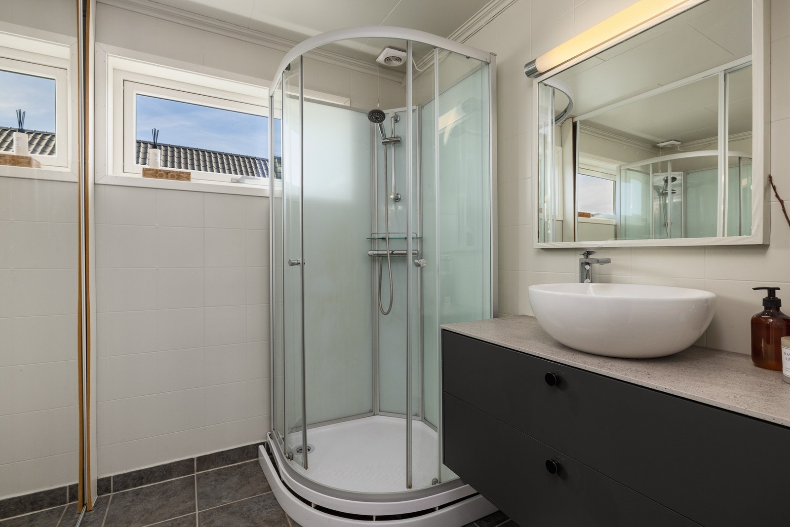 Badet er innredet med servantinnredning og dusjkabinett samt ekstra skapløsning for oppbevaring. Galleribilde