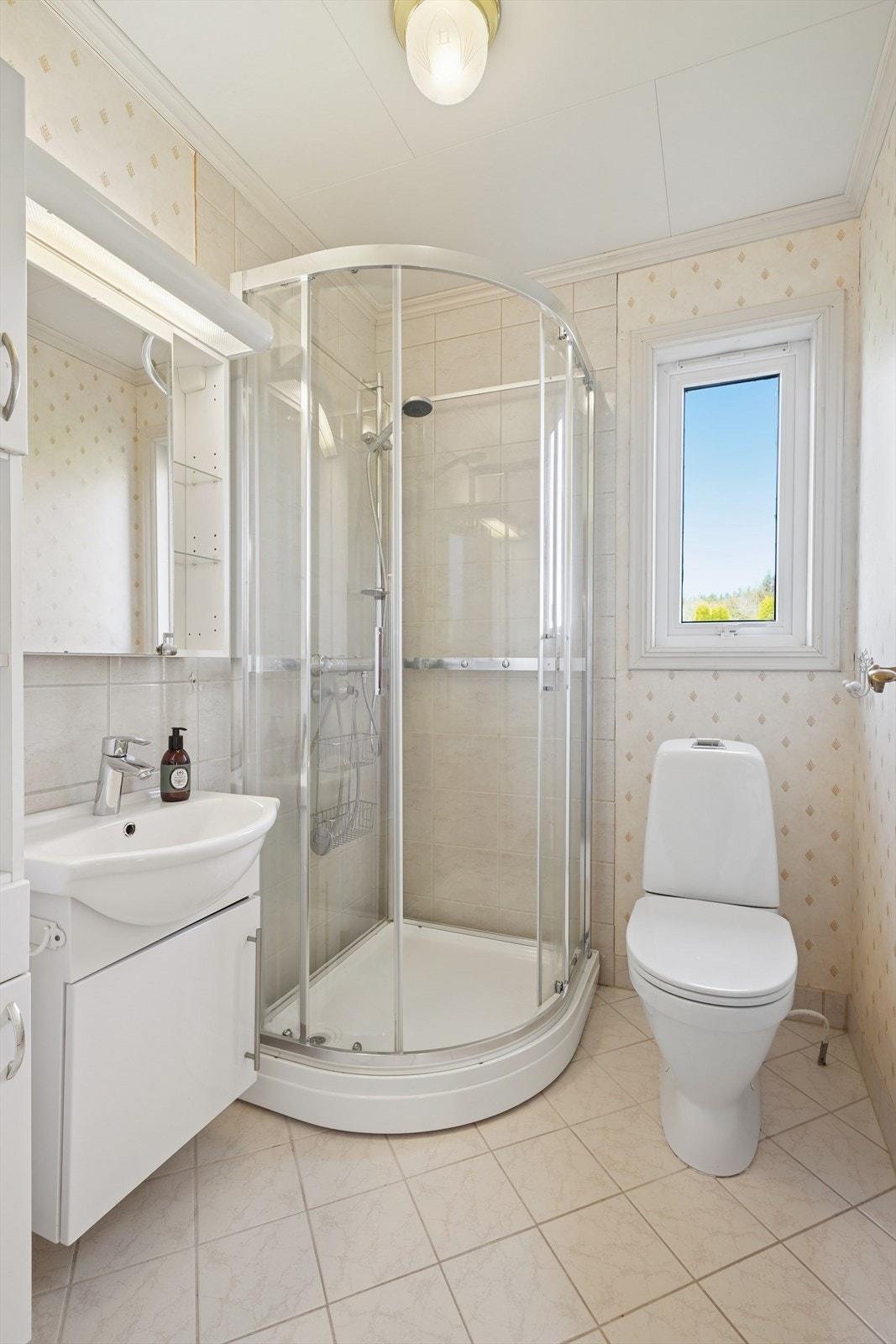 Badet er innredet med dusjkabinett, toalett og servant med underskap. Galleribilde