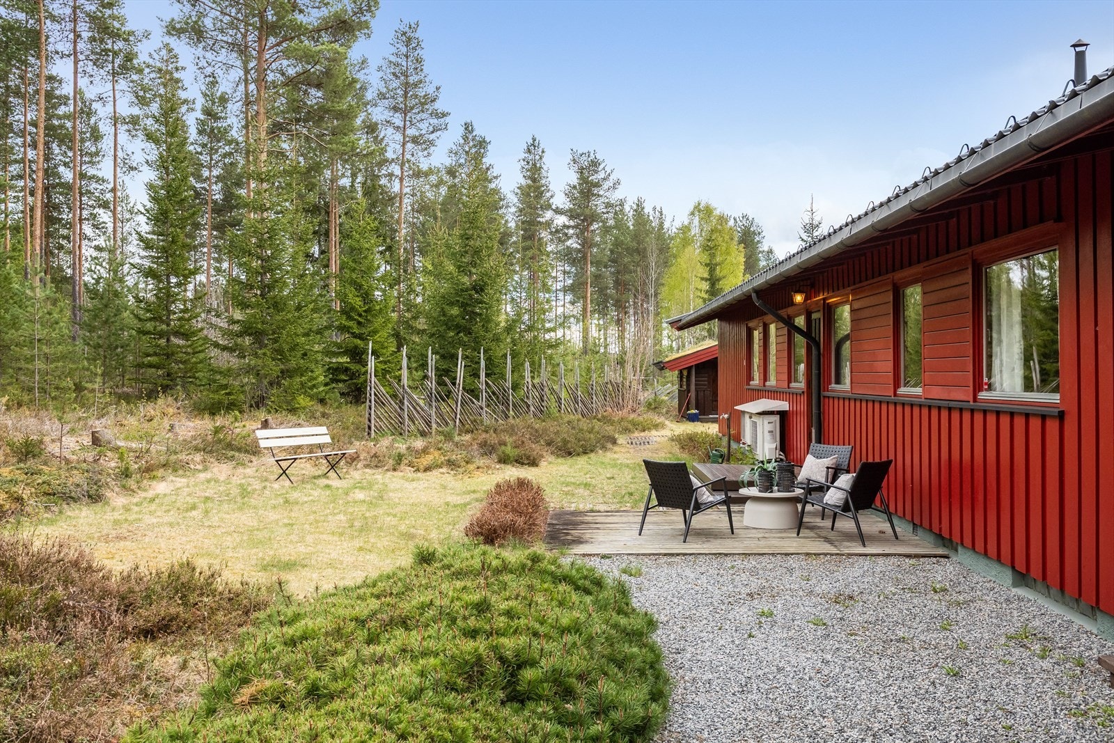 Koselig uteområde bak huset mot skogen, med terrasseplatting og sittebenk. Galleribilde