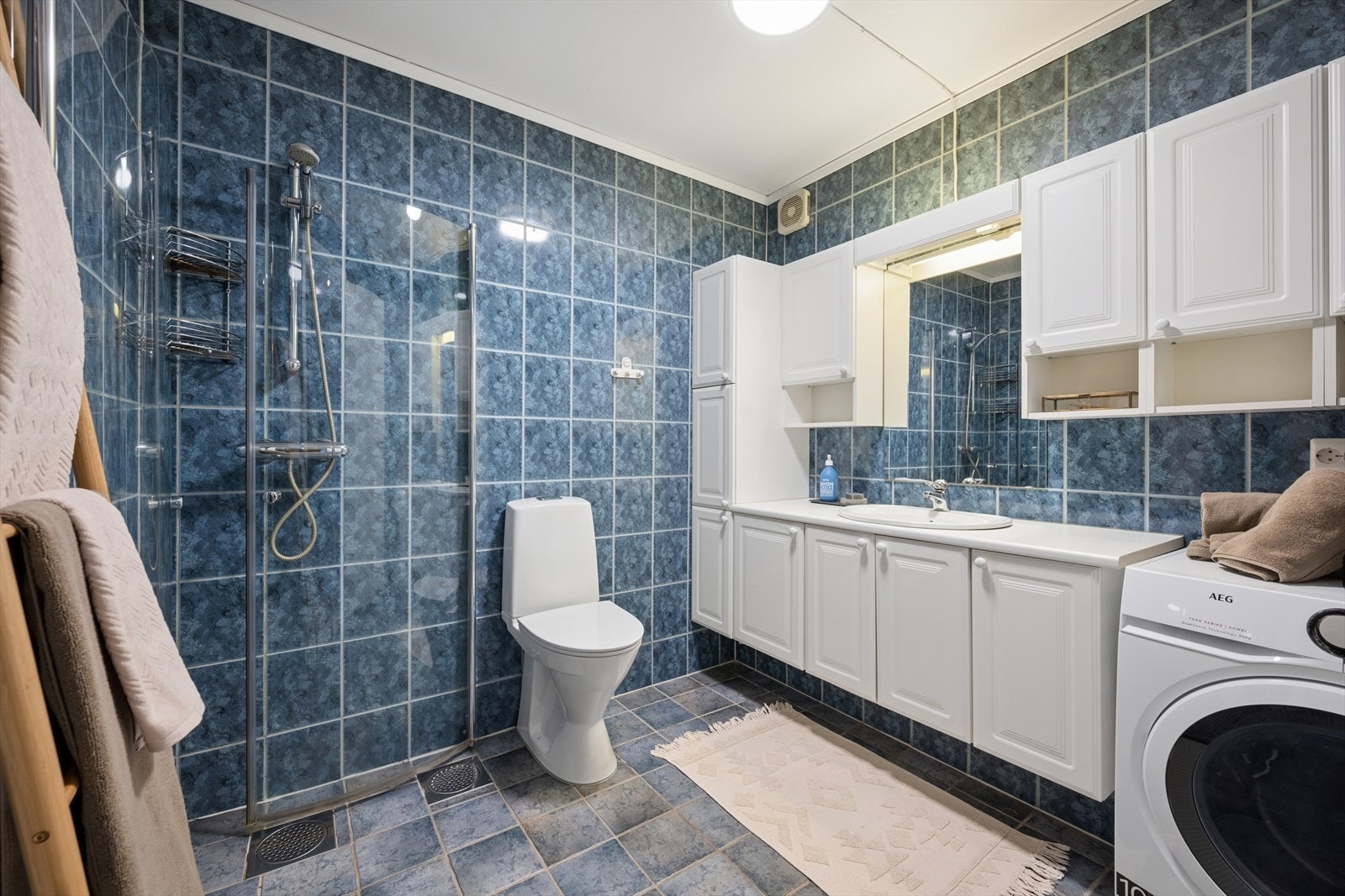Badet er romslig og praktisk innredet med flislagte vegger og gulv. Rommet er utstyrt med dusjhjørne med glassvegger, toalett og baderomsinnredning med god oppbevaringsplass og nedfelt servant. Galleribilde