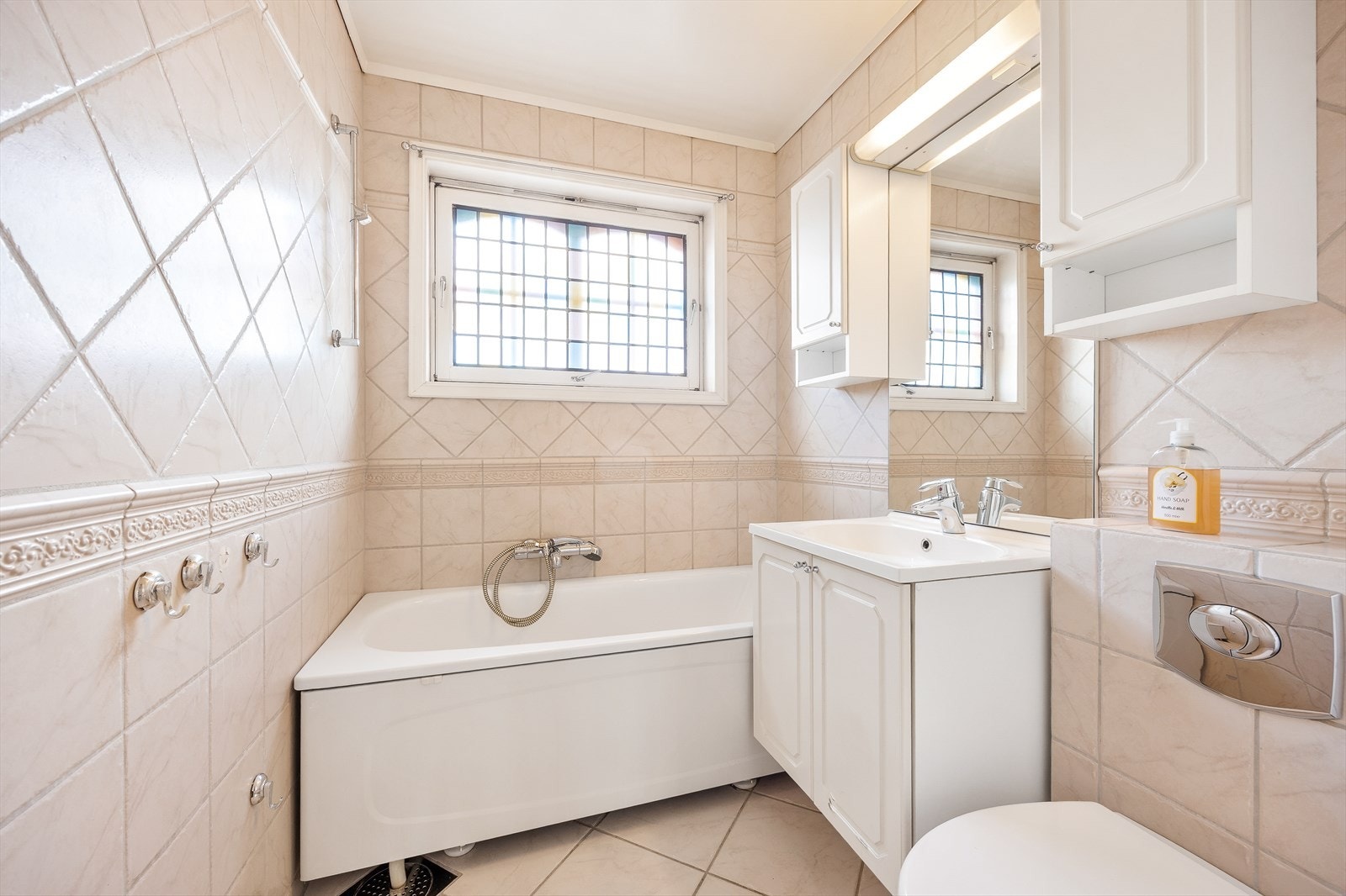 Badet i hovedetasjen har flislagte overflater og inneholder servant med innredning, speil med belysning, toalett og dusjløsning i badekar. Galleribilde
