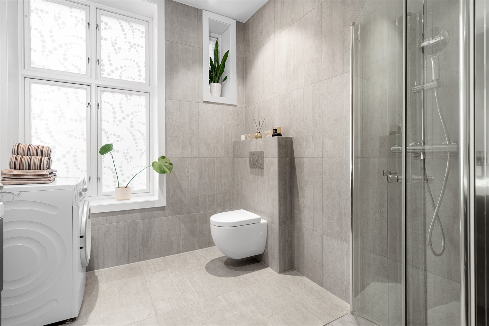Badet er utstyrt med vegghengt toalett og et dusjhjørne med svingbare glassdører. Galleribilde